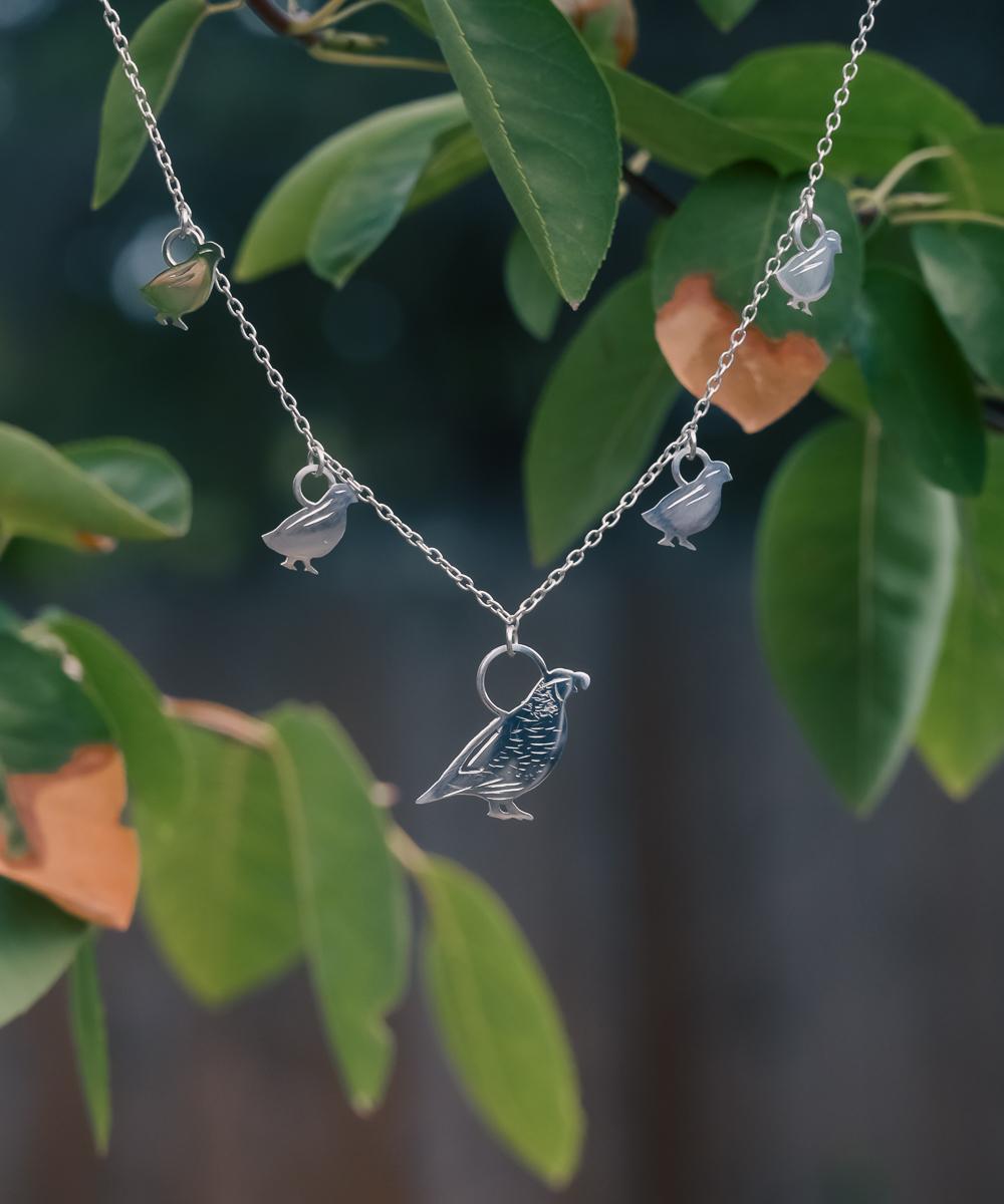 Silver necklace with 4 baby quail and 1 adult hanging from the middle representing a covey of quail. Button in top left of image reads FAUNAE and will take you to all animal themed pieces